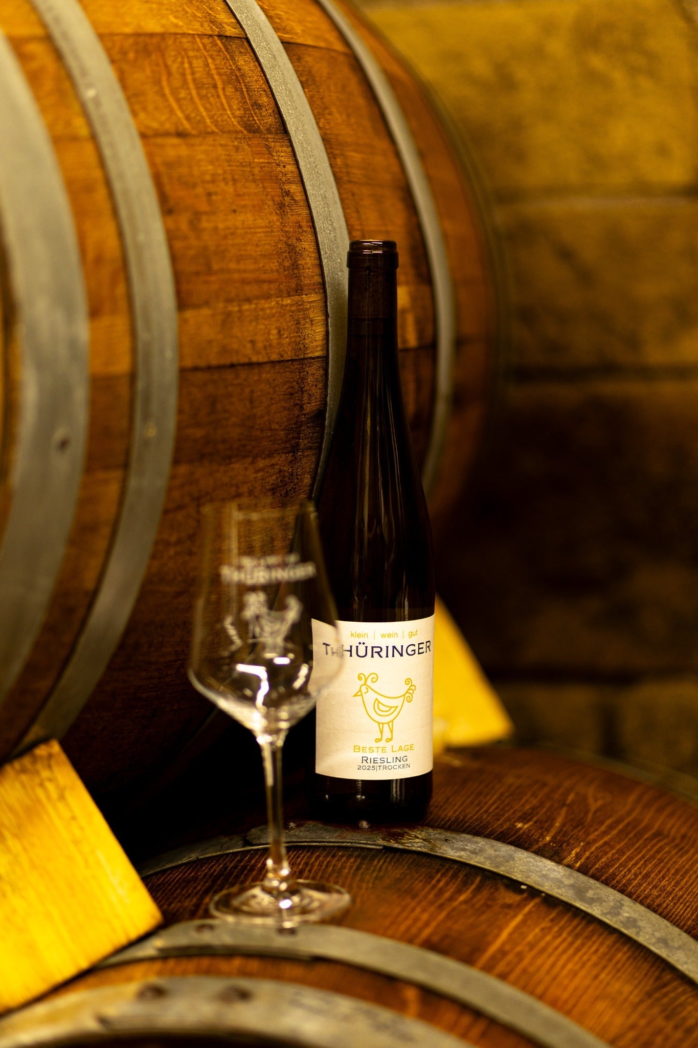 Rieslingflasche und Weinglas vor einem Holzfass im Weinkeller